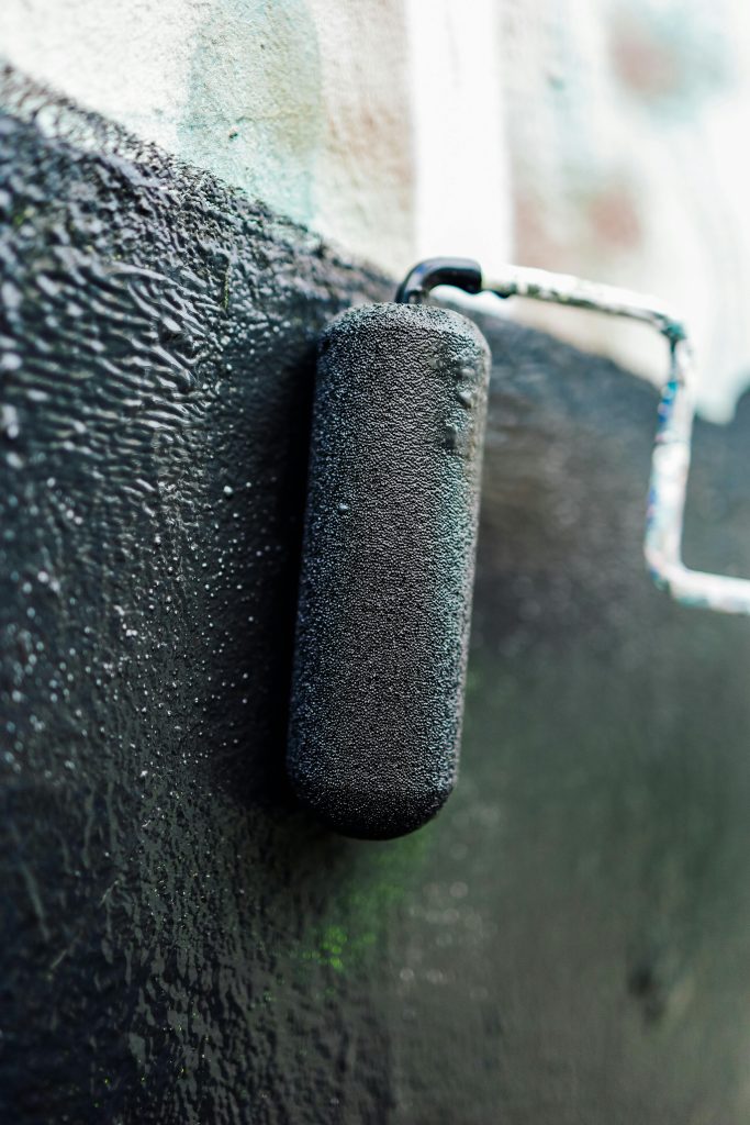 Detailed view of a paint roller applying fresh black paint on a surface, showcasing texture.